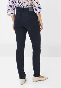 Marineblauwe jeans met een slanke pasvorm, gemaakt van een soepele stof. Heeft twee achterzakken en een merkembleem op de tailleband. Combinatie met lichtgekleurde schoenen.