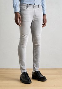 Šedé džíny s úzkým střihem z denimu s hladkou texturou, pětiprstým designem a zapínáním na knoflíky. Kombinovány s černými šněrovacími botami.