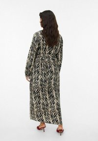 Robe maxi avec un imprimé abstrait noir et beige, dotée de manches longues, d'une ceinture et d'un design fluide. Portée avec des sandales à talons rouges.