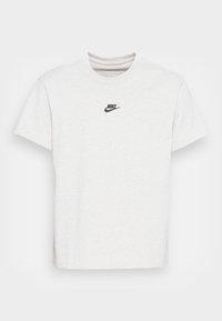 Jasnoszara bawełniana koszulka z okrągłym dekoltem, krótkimi rękawami i małym, czarnym logo Nike na piersi. Miękka tekstura, luźny krój.