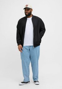 Schwarze Bomberjacke, weißes T-Shirt, hellblaue baggy Jeans, schwarz-weiße Sneaker und eine gestreifte Mütze mit Logo-Detail.