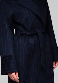 Abrigo de lana a rayas marino con solapas anchas, cinturón atado y puños doblados. Presenta rayas verticales y una tela suave y texturizada.