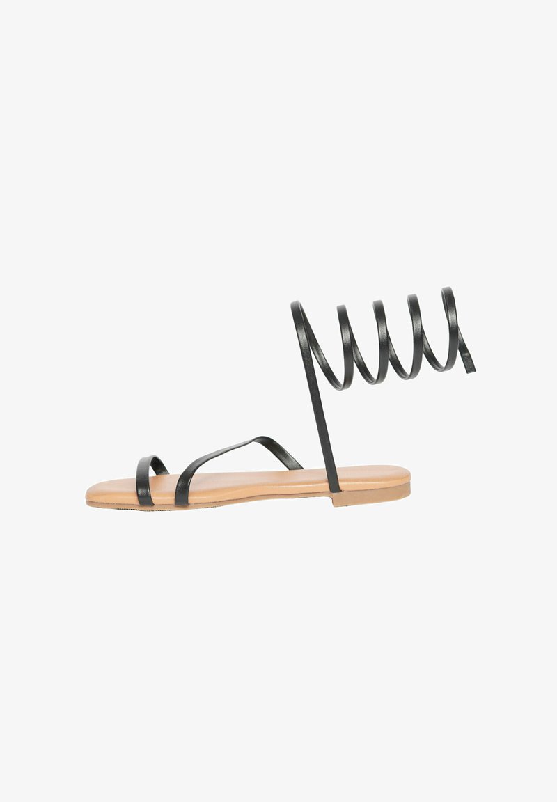 Sandali neri piatti con sottili spirali alla caviglia, design open-toe e suola di colore naturale. Le cinghie sono realizzate in un materiale liscio e opaco.