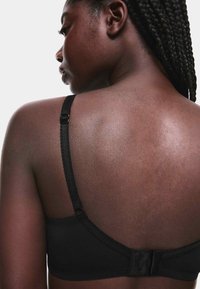 Soutien-gorge noir avec bretelles réglables, fermeture à agrafes, tissu lisse et bande large. Dispose de coutures décoratives le long des bords.