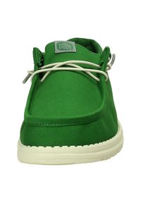 Scarpa slip-on in tela verde con suola in gomma bianca. Presenta lacci elastici, design a punta arrotondata e un'etichetta con scritto "The Dude".