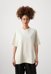 Ljusbeige oversized t-shirt i bomull, med rundad halsringning och korta ärmar. Subtil broderad detalj på bröstet.