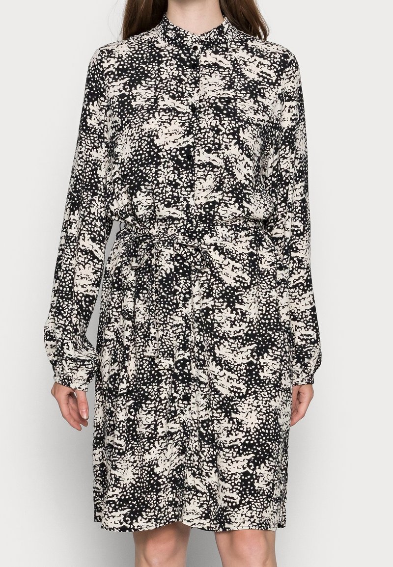 Robe à manches longues noire et blanche à imprimé abstrait, avec fermeture à boutons sur le devant et ceinture nouée assortie à la taille, portée à mi-cuisse.