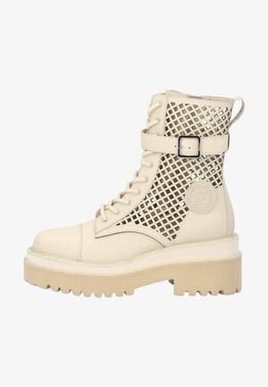 Bottine beige à lacets avec semelle épaisse en caoutchouc, côtés en maille, bride réglable avec boucle et écusson circulaire marqué sur le côté extérieur.