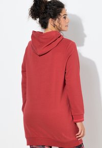 Czerwona bluza z kapturem o luźnym kroju, długimi rękawami i sznurkiem przy kapturze. Miękki materiał i rozcięcia po bokach nadają casualowy wygląd.