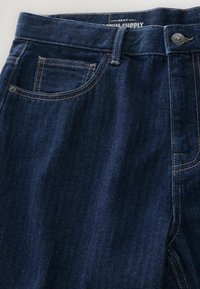 Ciemnoniebieskie dżinsy o gładkiej fakturze, z przednią kieszenią, kontrastowym przeszyciem i metalowym zapięciem w pasie.