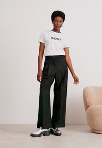 White T-shirt with "BOSS" print, black high-waisted trousers, and metallic platform shoes with a chunky sole. Simplistic and modern design.
