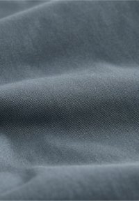 Gros plan sur un tissu bleu-gris lisse avec une texture de tissage diagonal fin et des plis doux créant des ombres douces.