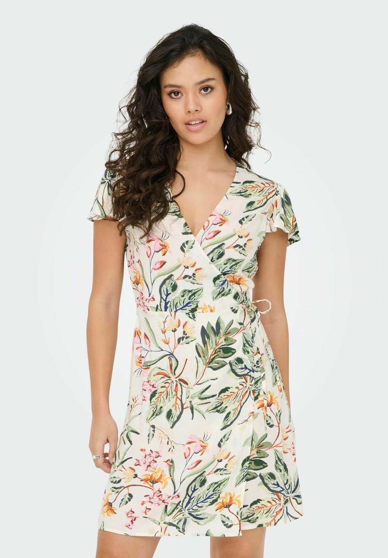 Vestido envolvente floral en beige claro con mangas cortas. Presenta patrones botánicos en colores vibrantes verde y rosa, con un detalle de lazo en el lado.