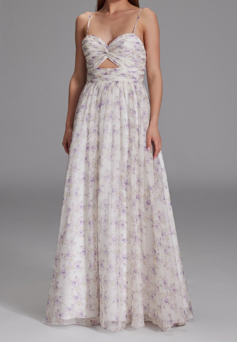 Abito lungo floreale in tessuto trasparente bianco con fiori viola e gialli. Presenta un corsetto aderente, dettaglio anteriore attorcigliato e spalline sottili.