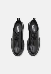 Black leather shoes with a glossy finish, featuring a rounded toe, lace-up design, and contrasting textured sole. Pull tab at the heel.