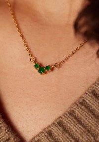 Gouden ketting met drie groene edelstenen die zijn gezet in ronde vingertjes. Glad, glanzend oppervlak met een verfijnd ontwerp.