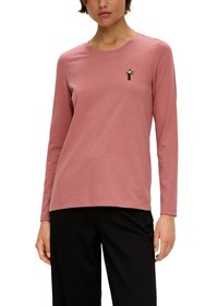 Różowa koszula bawełniana z długim rękawem i okrągłym dekoltem, z małą czarną i zieloną grafiką po lewej stronie klatki piersiowej. Gładka tekstura.