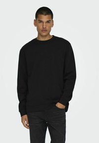Zwarte sweatshirt van een katoenmix met een ronde hals, lange mouwen en ribbels aan de mouwen en onderkant; gecombineerd met donkere jeans.