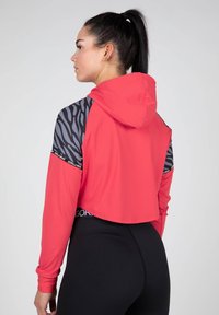 Gekürzter Kapuzenpullover in leuchtendem Pink mit schwarzen Zebra-Musterakzenten an den Ärmeln und "GORILLA WEAR"-Logo am Bund.