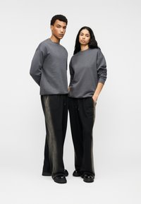 Γκρι φούτερ με στρογγυλή λαιμόκοψη, συνδυασμένα με άνετα μαύρα παντελόνια με διακριτικό σχέδιο. Μαύρα παπούτσια ολοκληρώνουν την εμφάνιση.