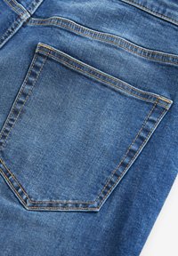 Denim jeans met een achterzak met dubbele stiksels in contrasterend oranje draad. Gladde textuur met een vervaagde blauwe kleur.