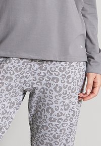 Gray long-sleeve top paired with gray leopard print pants. Soft fabric with a loose fit, featuring a subtle logo on the top’s hem.