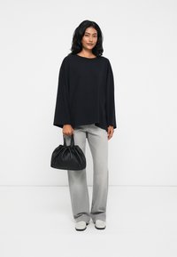 Μαύρη oversized μπλούζα με μακριά μανίκια, ανοιχτό γκρι παντελόνι σε φαρδιά γραμμή και μαύρη τσάντα με πτυχώσεις. Παπούτσια σε ανοιχτό γκρι χρώμα με μαύρη σόλα.