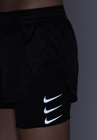 Svarta Nike löpning shortsen med ett vadderat ytterlager och inre åtsittande shorts. Har reflekterande Nike-logotypaccenter i tre rader.