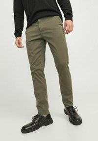 Chinos verde oliva hechos de una mezcla de algodón, con un corte ajustado, delantero plano y bolsillos delanteros, combinados con zapatos negros de cordones.