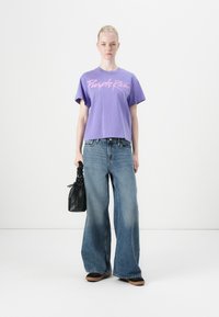 Purple cropped t-shirt with "Purple Rain" text in pink, paired with wide-leg blue denim jeans and a small black leather handbag.