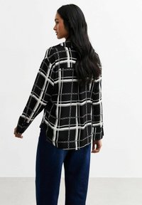 Camicia a quadri bianco e nero con maniche lunghe, polsini abbottonati e vestibilità comoda. Il design include dettagli a motivo catena in tutto il capo.