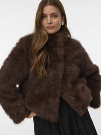 Brun cropped jakke i imiteret pels med høj krave, prydet med tekstureret overflade og brede ærmer, kombineret med en sort kjole.