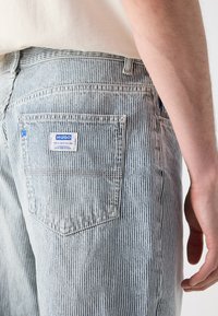 Csíkos, világoskék farmernadrág texturált felülettel. Látható hátsó zseb kék logó címkével. Kényelmes, laza szabás.