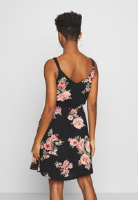 Robe noire à fleurs avec bretelles spaghetti, présentant un dos en V. Décorée de grandes roses roses et rouges, cintrée à la taille.
