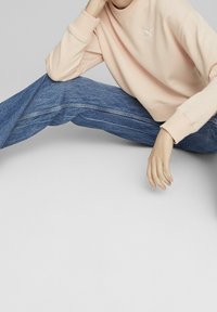 Felpa rosa chiaro con scollatura rotonda e logo ricamato, abbinata a jeans in denim blu. I jeans hanno una vestibilità dritta e un leggero sbiadimento.