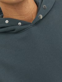 Mørk teal hoodie med struktureret stof. Har sølvfarvede trykknapper ved halsudskæringen og en afslappet pasform, der fremhæver det bløde stof.