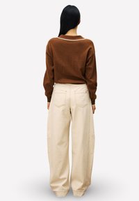 Pull en tricot marron avec un décolleté au dos en forme de U, associé à un pantalon beige ample avec poches et une coupe large.