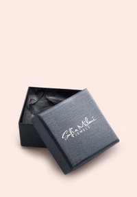 Svart texturerad smyckeslåda, något öppen, som avslöjar skrynkligt svart silkespapper inuti. "Sofia Milani Jewels" tryckt i vitt på locket.
