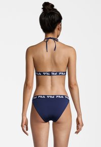 Costume da bagno blu Navy composto da un reggiseno a halter con chiusura a lacci e fascia con logo. La parte inferiore presenta una fascia coordinata con un sottile dettaglio del logo.