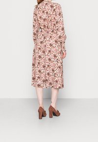 Blommönstrad midiklänning i mjukt, lätt material med långa ärmar, åtsittande midja och lös passform, tillsammans med bruna mockablockklackskor.