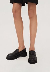 Czarne skórzane mokasyny z masywną, ryflowaną podeszwą, wyposażone w szeroki pasek na przodzie i gładkie wykończenie.