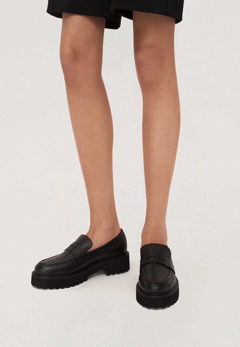 Czarne skórzane mokasyny z masywną, ryflowaną podeszwą, wyposażone w szeroki pasek na przodzie i gładkie wykończenie.