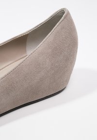 Chaussure compensée en daim beige avec talon fermé et bout arrondi, vue de côté en angle sur fond blanc.