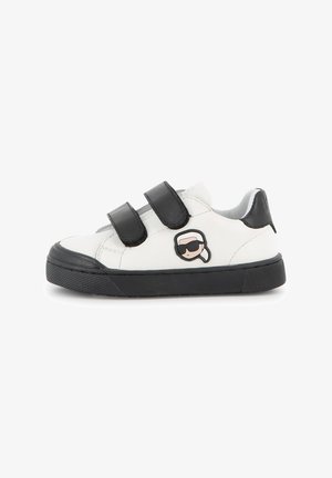 Baskets blanches pour enfants avec semelle noire et deux bandes velcro noires, avec un petit visage de dessin animé avec des lunettes de soleil sur le côté.