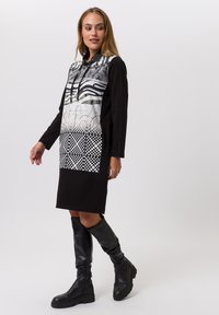 Robe noire à manches longues avec un devant à motif en gris et blanc. Le design comprend des rayures, des points et des formes abstraites.