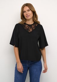 Sort kortærmet bluse med en blondeindsats V-udskæring, et tekstureret stof og afslappet pasform. Kombineret med blå denimjeans.