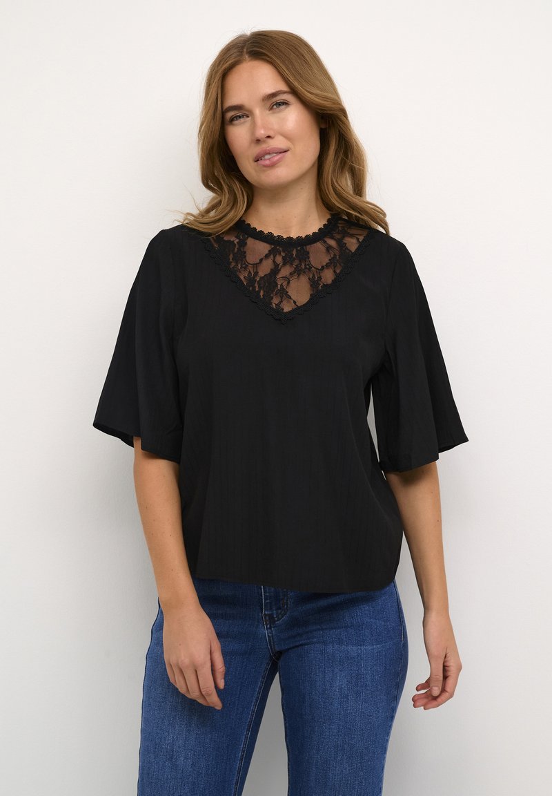 Sort kortærmet bluse med en blondeindsats V-udskæring, et tekstureret stof og afslappet pasform. Kombineret med blå denimjeans.