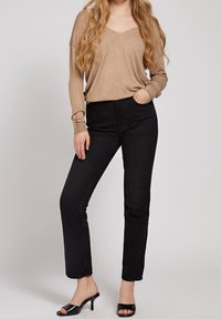 Maglione beige a maglia con scollatura a V, abbinato a jeans neri a gamba dritta e tacchi neri open-toe. L'outfit presenta uno stile rilassato.