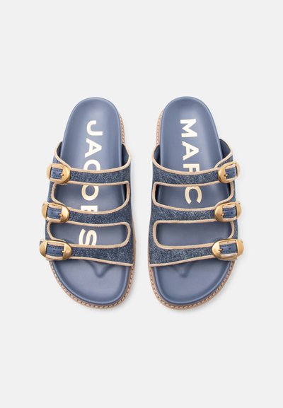 Ζευγάρι μπλε σανδαλιών με τρεις ρυθμιζόμενους ιμάντες από τζιν και χρυσές αγκράφες, μπλε πάτος και μπεζ περιθώριο σε λευκό φόντο.