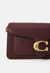 Burgundy pebbled leather wallet with gold-tone clasp shaped like the letter C on a white background.